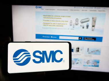 Stuttgart, Germany - 07-25-2024: Person holding smartphone with logo of Japanese machinery company SMC Corporation in front of website. Focus on phone display. clipart