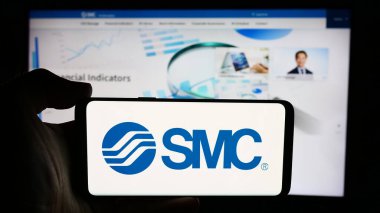 Stuttgart, Almanya - 07-25-2024: Japon makine şirketi SMC Corporation 'ın logosuyla cep telefonu sahibi kişi iş sayfasının önünde. Telefon ekranına odaklan.