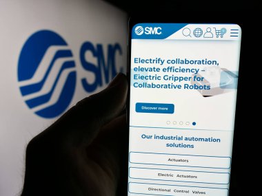 Stuttgart, Almanya - 07-25-2024: Japon makine şirketi SMC Corporation 'ın web sayfası ile iş logosu önünde akıllı telefon tutan kişi. Telefon ekranının merkezine odaklan.