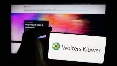 Stuttgart, Almanya - 07-25-2024: Hollandalı bilgi hizmetleri şirketi Wolters Kluwer N.V. 'nin logosuna sahip akıllı telefon sahibi kişi web sitesi önünde. Telefon ekranına odaklan.