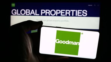 Stuttgart, Germany - 07-25-2024: Person holding cellphone with logo of Australian property company Goodman Group in front of business webpage. Focus on phone display. clipart