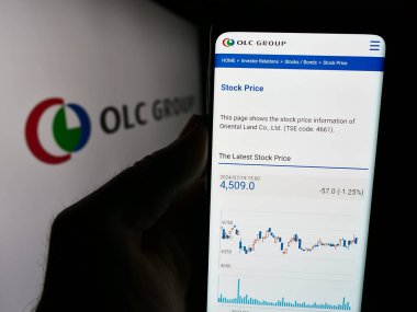 Stuttgart, Almanya - 07-25-2024: Japon turizm şirketi Oriental Land Co. Ltd. (OLC) 'nin internet sayfası ile logo önünde cep telefonu tutan kişi. Telefon ekranının merkezine odaklan.