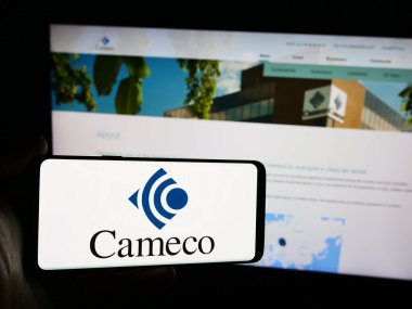 Stuttgart, Almanya - 07-21-2024: Kanadalı uranyum madencilik şirketi Cameco Corporation 'ın logosunun bulunduğu cep telefonu sahibi kişi iş sayfasının önünde. Telefon ekranına odaklan.