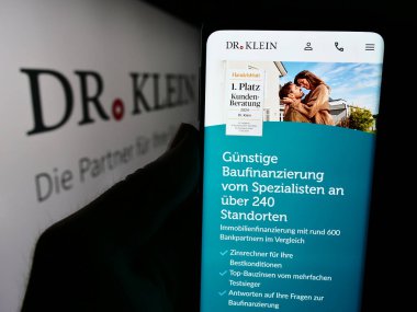 Stuttgart, Almanya - 07-21-2024: Alman mali danışmanlık şirketi Dr. Klein Co. AG 'nin logo önündeki web sayfası ile cep telefonu tutan kişi. Telefon ekranının merkezine odaklan.