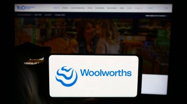 Stuttgart, Almanya - 07-21-2024: Avustralyalı perakende şirketi Woolworths Group Limited 'in logosuna sahip cep telefonu sahibi kişi iş sayfası önünde bulunuyor. Telefon ekranına odaklan.
