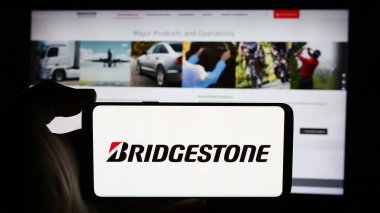 Stuttgart, Almanya - 07-21-2024: Japon lastik şirketi Bridgestone Corporation 'ın logosuyla cep telefonu tutan kişi iş sayfasının önünde. Telefon ekranına odaklan.