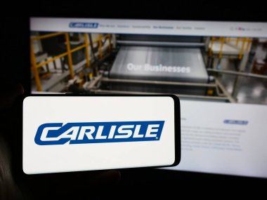 Stuttgart, Almanya - 07-21-2024: Web sayfası önünde inşaat malzemeleri şirketi Carlisle Şirketleri 'nin logosuna sahip cep telefonu sahibi kişi. Telefon ekranına odaklan.