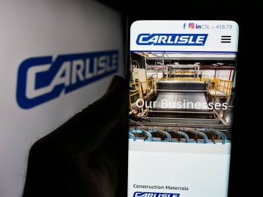 Stuttgart, Almanya - 07-21-2024: İnşaat malzemeleri şirketi Carlisle Şirketi 'nin logolu web sayfası ile cep telefonu tutan kişi. Telefon ekranının merkezine odaklan.