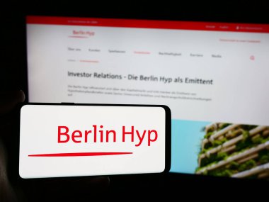 Stuttgart, Almanya - 07-21-2024: Üzerinde Alman mortgage bankacılık şirketi Berlin Hyp AG 'nin logosu olan cep telefonu bulunduran kişi iş sayfasının önünde. Telefon ekranına odaklan.