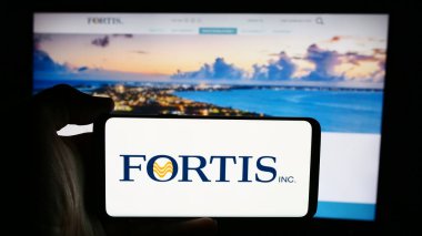 Stuttgart, Almanya - 07-23-2024: Kanadalı elektrik şirketi Fortis Inc. 'in logosuyla cep telefonu tutan kişi iş sayfasının önünde. Telefon ekranına odaklan.