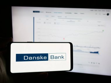 Stuttgart, Almanya - 07-23-2024: Danimarkalı finans hizmetleri şirketi Danske Bank AS 'nin logosuyla cep telefonu sahibi olan kişi iş sayfasının önünde. Telefon ekranına odaklan.