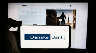 Stuttgart, Almanya - 07-23-2024: Danimarkalı finans hizmetleri şirketi Danske Bank AS 'nin logosuyla cep telefonu tutan kişi iş sayfasının önünde. Telefon ekranına odaklan.