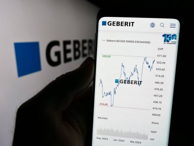 Stuttgart, Almanya - 07-23-2024: İsviçre sağlık ürünleri şirketi Geberit AG 'nin web sitesi ile logo önünde cep telefonu tutan kişi. Telefon ekranının merkezine odaklan.