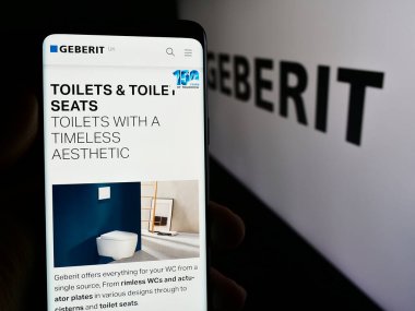 Stuttgart, Almanya - 07-23-2024: İsviçreli hijyen ürünleri şirketi Geberit AG 'nin internet sayfası ile iş logosu önünde cep telefonu tutan kişi. Telefon ekranının merkezine odaklan.