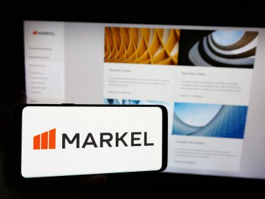 Stuttgart, Germany - 07-23-2024: Person holding smartphone with logo of US specialty insurance company Markel in front of website. Focus on phone display. clipart