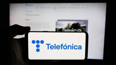 Stuttgart, Almanya - 07-23-2024: İspanyol telekomünikasyon şirketi Telefonica S.A. 'nın logosuyla cep telefonu tutan kişi iş sayfası önünde. Telefon ekranına odaklan.