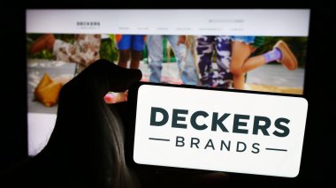 Stuttgart, Almanya - 07-23-2024: İnternet sitesi önünde ABD 'li ayakkabı şirketi Deckers Outdoor Corporation' ın logosunu taşıyan kişi. Telefon ekranına odaklan.