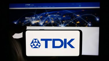 Stuttgart, Almanya - 07-23-2024: Japon elektronik şirketi TDK Corporation 'ın logosuyla cep telefonu sahibi kişi iş sayfasının önünde. Telefon ekranına odaklan.