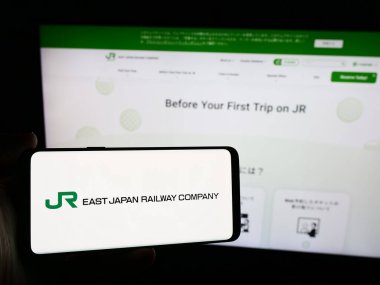 Stuttgart, Almanya - 07-23-2024: İnternet sitesinin önünde Japon demiryolu işletmesi Doğu Japonya Demiryolu Şirketi 'nin logosuna sahip kişi. Telefon ekranına odaklan.