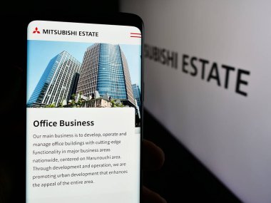Stuttgart, Almanya - 07-23-2024: Japon emlak şirketi Mitsubishi Estate Co. Ltd. (MEC) 'nin logolu web sayfası ile cep telefonu tutan kişi. Telefon ekranının merkezine odaklan.