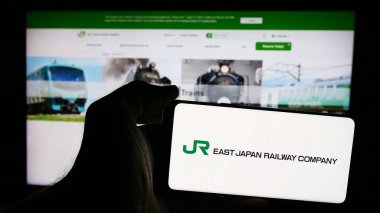 Stuttgart, Almanya - 07-23-2024: Japon demiryolu şirketi Doğu Japonya Demiryolu Şirketi 'nin logosuna sahip cep telefonu sahibi kişi web sitesinin önünde. Telefon ekranına odaklan.