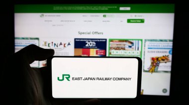 Stuttgart, Almanya - 07-23-2024: Japon demiryolu şirketi Doğu Japonya Demiryolu Şirketi 'nin logosuyla cep telefonu sahibi kişi iş sayfasının önünde. Telefon ekranına odaklan.