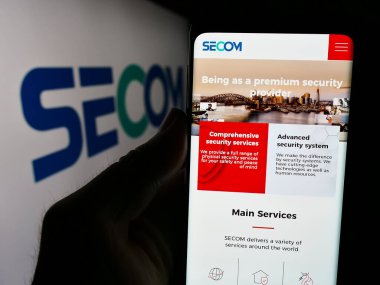 Stuttgart, Almanya - 07-24-2024: Japon güvenlik şirketi Secom Co. Ltd. nin internet sayfası ile cep telefonu tutan kişi iş logosu önünde. Telefon ekranının merkezine odaklan.