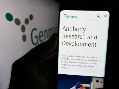 Stuttgart, Germany - 07-24-2024: Person holding cellphone with webpage of Danish biotechnology company Genmab AS in front of business logo. Focus on center of phone display. clipart