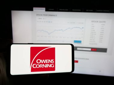 Stuttgart, Almanya - 07-24-2024: Amerikan inşaat malzemeleri şirketi Owens Corning 'in logosunun bulunduğu cep telefonu sahibi kişi iş sayfasının önünde. Telefon ekranına odaklan.