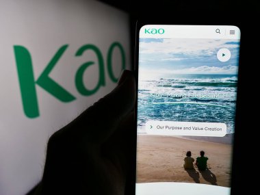 Stuttgart, Almanya - 07-24-2024: Japon kimya şirketi Kao Corporation 'ın internet sayfası ile birlikte iş logosu önünde cep telefonu tutan kişi. Telefon ekranının merkezine odaklan.