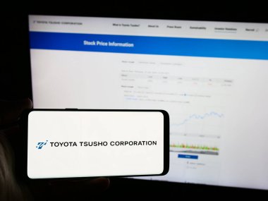 Stuttgart, Almanya - 07-25-2024: Japon ticaret şirketi Toyota Tsusho Corporation 'ın logosunun bulunduğu cep telefonu sahibi kişi iş sayfasının önünde. Telefon ekranına odaklan.