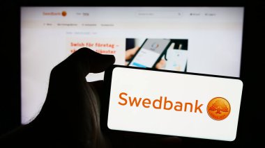 Stuttgart, Almanya - 07-25-2024: İsveçli finans hizmetleri şirketi Swedbank AB 'nin logosunun bulunduğu akıllı telefon sahibi kişi web sitesi önünde. Telefon ekranına odaklan.