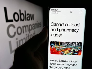 Stuttgart, Almanya - 07-25-2024: Kanadalı perakende şirketi Loblaw Companies Ltd. 'nin internet sayfası ile logo önünde cep telefonu tutan kişi. Telefon ekranının merkezine odaklan.