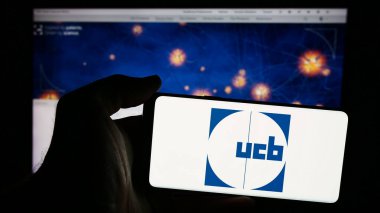 Stuttgart, Almanya - 07-25-2024: Belçikalı biyofarmasötik şirketi UCB S.A. 'nın logosuna sahip akıllı telefon sahibi kişi web sitesi önünde. Telefon ekranına odaklan.