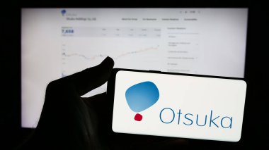 Stuttgart, Almanya - 07-29-2024: Japon şirketi Otsuka Pharmaceutical Co. Ltd. 'nin logosunun bulunduğu cep telefonu sahibi kişi iş sayfasının önünde. Telefon ekranına odaklan.