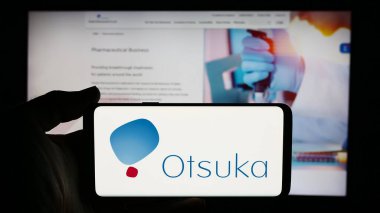 Stuttgart, Almanya - 07-29-2024: Japon Otsuka Pharmaceutical Co. Ltd. şirketinin logosuyla cep telefonu tutan kişi iş sayfasının önünde. Telefon ekranına odaklan.
