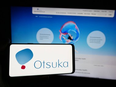 Stuttgart, Almanya - 07-29-2024: Japon şirketi Otsuka Pharmaceutical Co. Ltd. nin logosuna sahip akıllı telefon sahibi kişi web sitesinin önünde. Telefon ekranına odaklan.