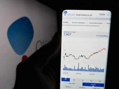Stuttgart, Almanya - 07-29-2024: Japon şirketi Otsuka Pharmaceutical Co. Ltd. logo önünde cep telefonu tutan kişi. Telefon ekranının merkezine odaklan.