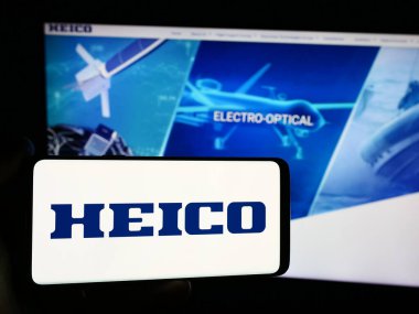 Stuttgart, Almanya - 07-29-2024: Amerikan havacılık şirketi HEICO Corporation 'ın logosunun bulunduğu cep telefonu sahibi kişi iş sayfasının önünde. Telefon ekranına odaklan.