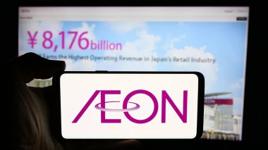 Stuttgart, Almanya - 07-29-2024: Japon perakende şirketi Aeon Co. Ltd. 'nin logosuna sahip cep telefonu sahibi kişi iş sayfasının önünde. Telefon ekranına odaklan.