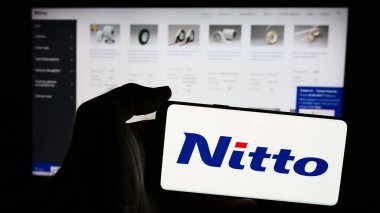 Stuttgart, Germany - 07-29-2024: Person holding smartphone with logo of Japanese chemical company Nitto Denko Corporation in front of website. Focus on phone display. clipart