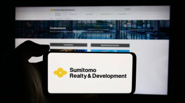 Stuttgart, Germany - 07-29-2024: Person holding cellphone with logo of Japanese ocmpany Sumitomo Realty Development Co. Ltd. in front of business webpage. Focus on phone display. clipart