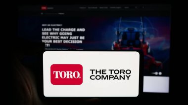 Stuttgart, Almanya - 07-30-2024: ABD 'li çim biçme makinesi şirketi logosu olan cep telefonu sahibi kişi The Toro Company iş sayfasının önünde. Telefon ekranına odaklan.