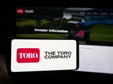 Stuttgart, Almanya - 07-30-2024: ABD 'li çim biçme makinesi şirketi logosu olan akıllı telefon sahibi kişi The Toro Company web sitesinin önünde. Telefon ekranına odaklan.
