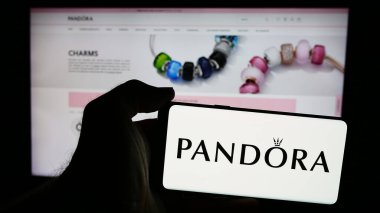 Stuttgart, Almanya - 07-30-2024: Danimarkalı mücevher şirketi Pandora AS 'nin logosunun bulunduğu akıllı telefonu web sitesinin önünde tutan kişi. Telefon ekranına odaklan.
