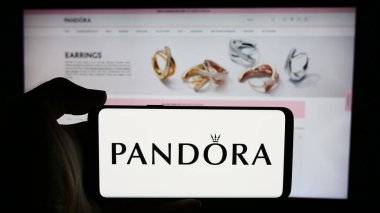 Stuttgart, Almanya - 07-30-2024: Danimarkalı mücevher şirketi Pandora AS 'nin logosuyla cep telefonu tutan kişi iş sayfasının önünde. Telefon ekranına odaklan.