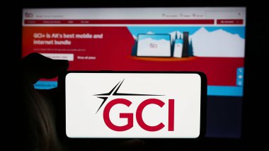 Stuttgart, Almanya - 07-31-2024: ABD 'li telekomünikasyon şirketi GCI Communication Corp' un logosuyla cep telefonu sahibi kişi iş sayfası önünde. Telefon ekranına odaklan.