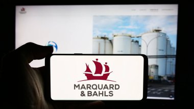 Stuttgart, Almanya - 07-31-2024: Alman enerji şirketi Marquard ve Bahls AG 'nin logosuna sahip cep telefonu sahibi kişi iş sayfasının önünde. Telefon ekranına odaklan.