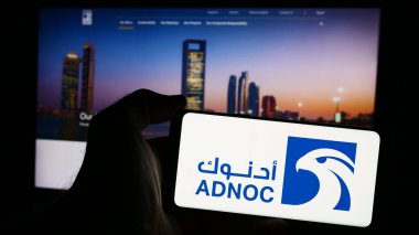 Stuttgart, Almanya - 08-12-2024: İnternet sayfası önünde üzerinde Abu Dabi Ulusal Petrol Şirketi (ADNOC) logosu bulunan cep telefonu sahibi kişi. Telefon ekranına odaklan.