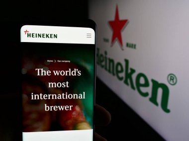 Stuttgart, Almanya - 08-12-2024: Hollandalı bira şirketi Heineken N.V. 'nin web sayfası ile iş logosu önünde akıllı telefon tutan kişi. Telefon ekranının merkezine odaklan.